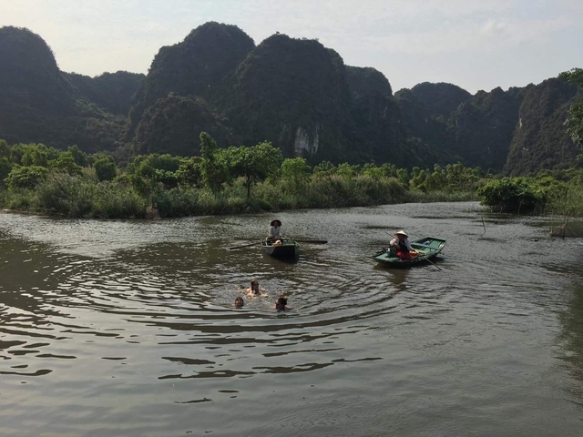 A small group swimming and boating in a river with mountains.