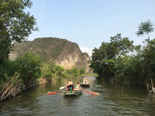 People rowing boats through scenic landscape with cliffs.