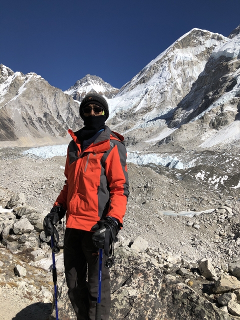 Person in a red jacket standing in a mountainous area with snow-covered peaks.