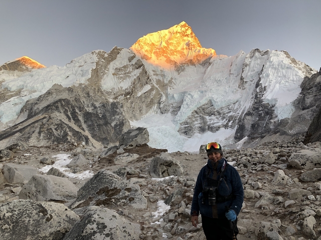 Person standing in front of snowy mountains at sunset.