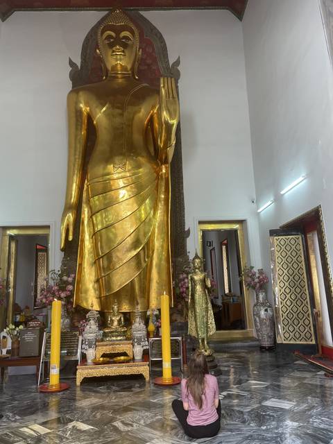 Woman praying in front of a large golden Buddha statue.