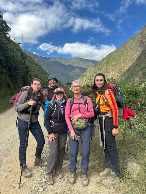 Five hikers dressed in gear standing on a trail surrounded by mountains.