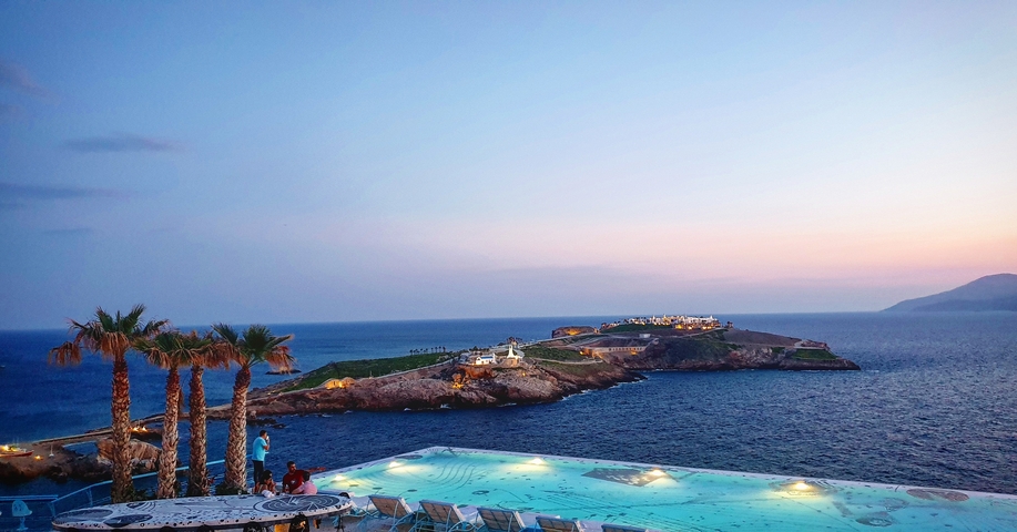 Infinity pool overlooking the ocean at sunset with island view.