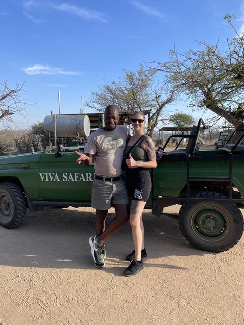 Two people standing by a safari vehicle in a desert environment.