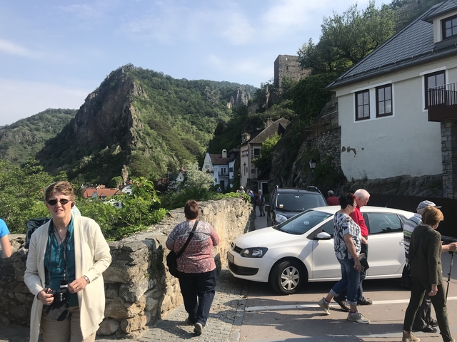 People walking along a scenic town path with hills in the background.