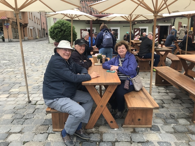 Three people sitting at an outdoor table in a cobblestone square.