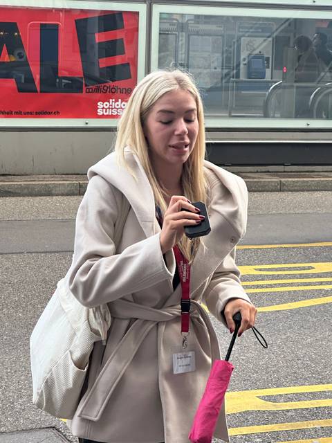       Person with a phone and an umbrella at a station.
  
