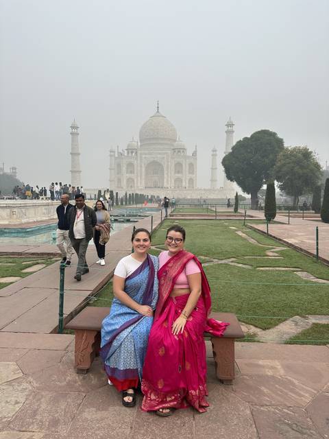 Two women in colorful dresses sitting in front of the Taj Mahal.