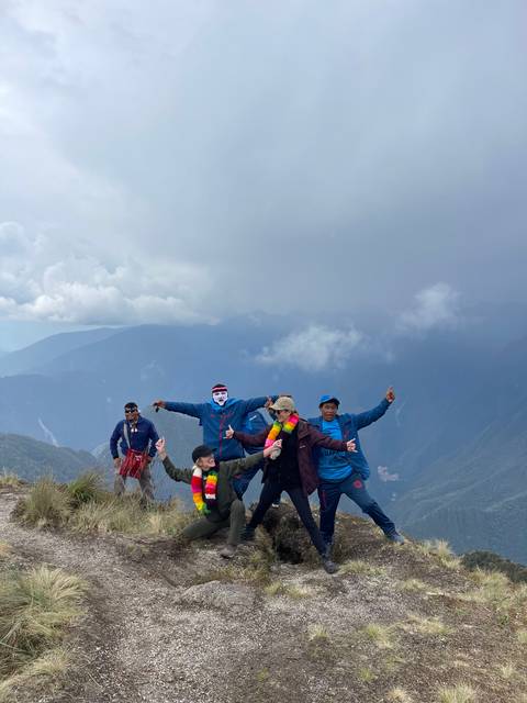       People posing on a mountain path with cloudy background.
  