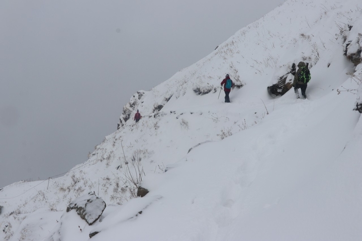 Hikers trekking through snow in a mountainous landscape.