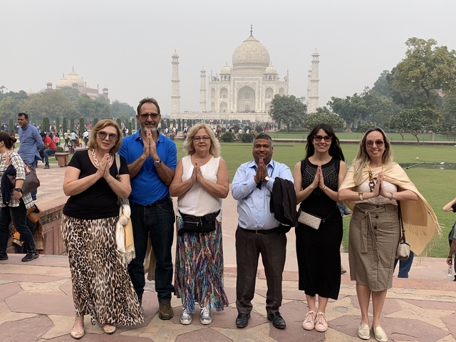       Group posing with folded hands in front of the Taj Mahal.
  