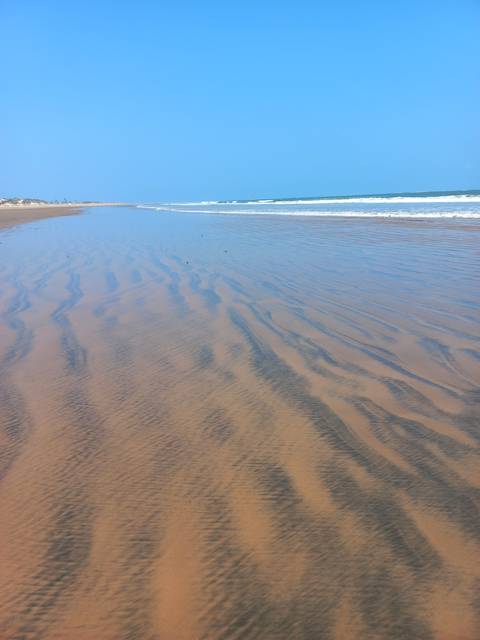       Sandy beach with waves under a clear blue sky.
  