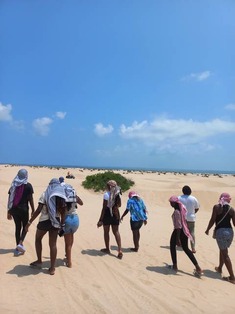       Group of people walking on a sandy path by the sea.
  