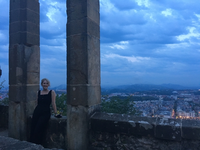 Woman posing between two stone columns with a city view below.
