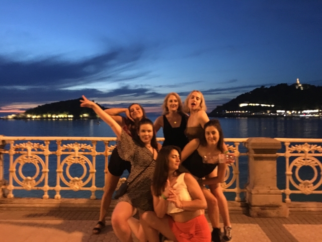 Group of women posing joyfully in front of a waterfront at sunset.