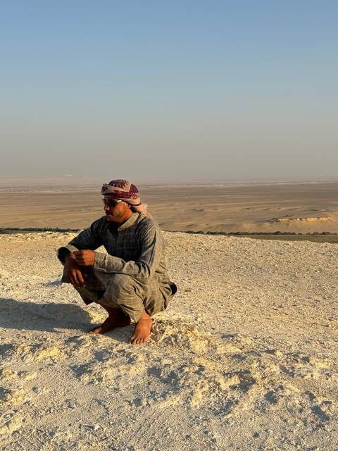      Person crouching on a rocky surface overlooking a desert.
  