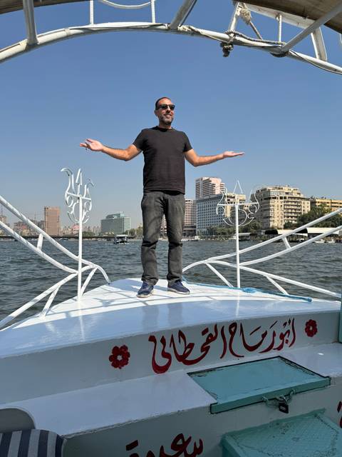       Man standing elegantly on a boat with city skyline in the background.
  