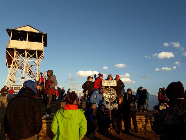 Crowd gathered at a high-altitude viewpoint with snow-capped mountains.