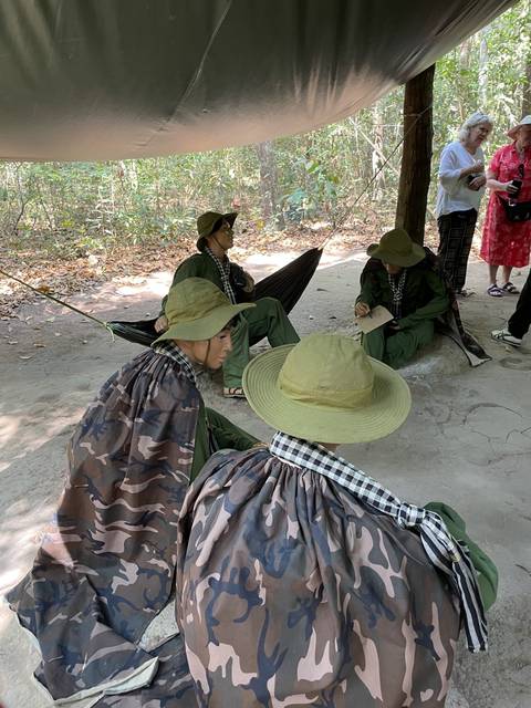       People sitting under a canopy wearing traditional hats.
  