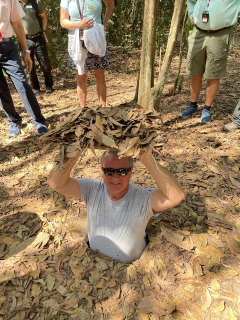       Person emerging from a hole in the ground covered in leaves.
  
