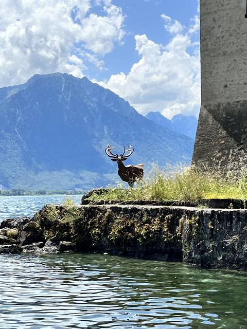       Sculpture of a deer in front of a lake and mountains.
  