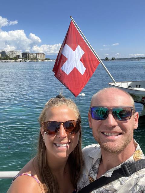       Couple posing with a Swiss flag on a boat on the water.
  