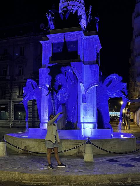       Person standing near a blue-lit monument in a city square.
  
