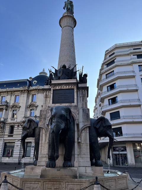       Monument with statues of elephants in a city center under a clear sky.
  