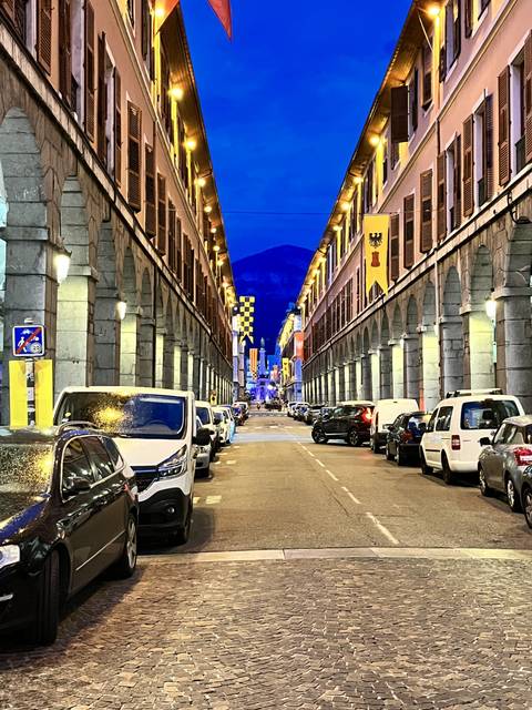      Illuminated street view during the evening with buildings and cars.
  