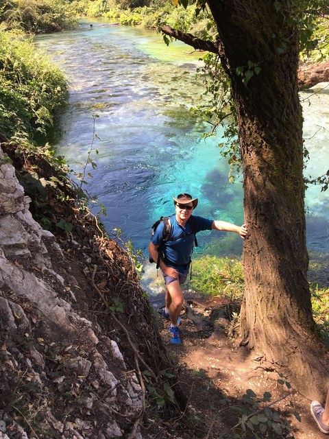 Man hiking next to a vibrant blue river.