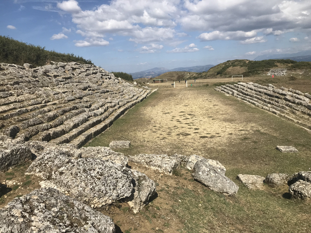 Ancient amphitheater with stone seats in a rural landscape.