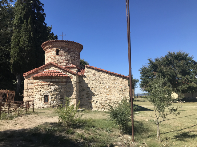       Small stone chapel with a red-tiled roof under clear sky.
  