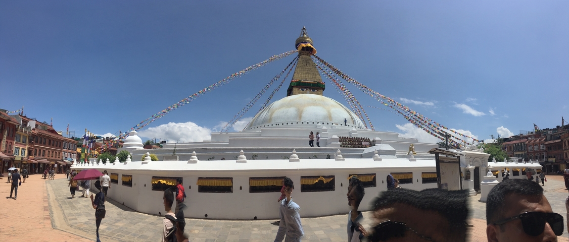 Large stupa with prayer flags and people walking around.