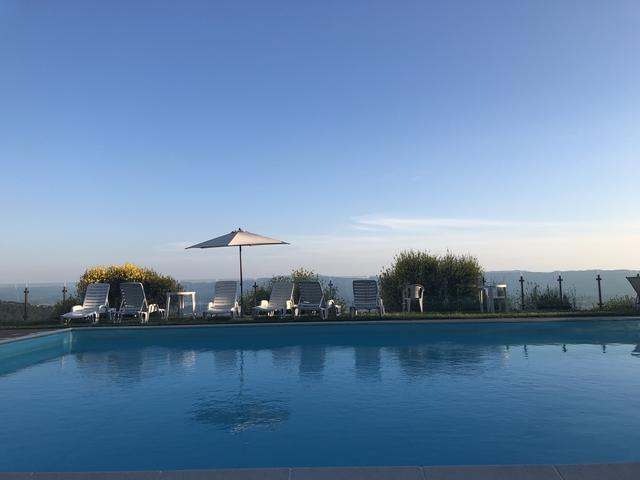 Swimming pool area with loungers and a scenic view over a valley.