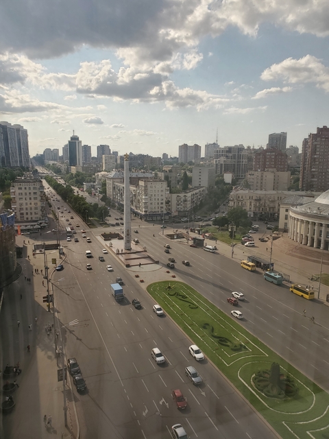 View of a city intersection with tall buildings and a monument.