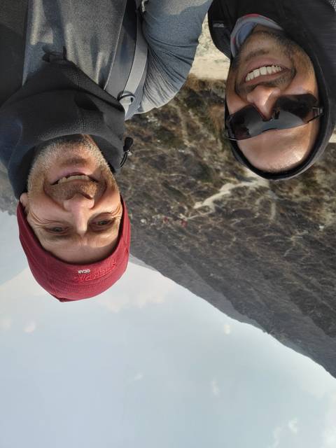 Two people posing with mountains and trails in the background.