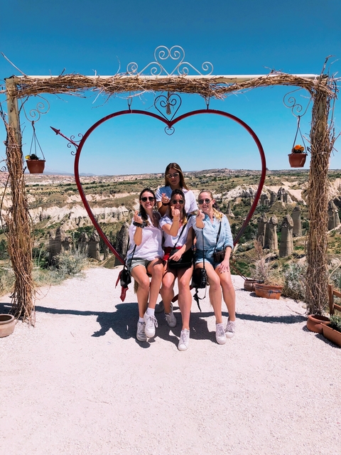 Women sitting on a heart-shaped swing with a scenic view.