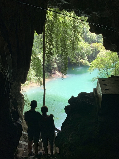       Cave entrance opening to a green river.
  