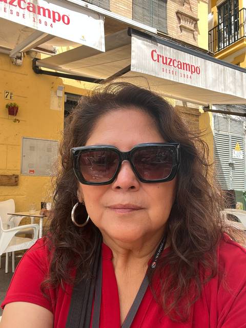       A woman with sunglasses posing outside a cafe.
  