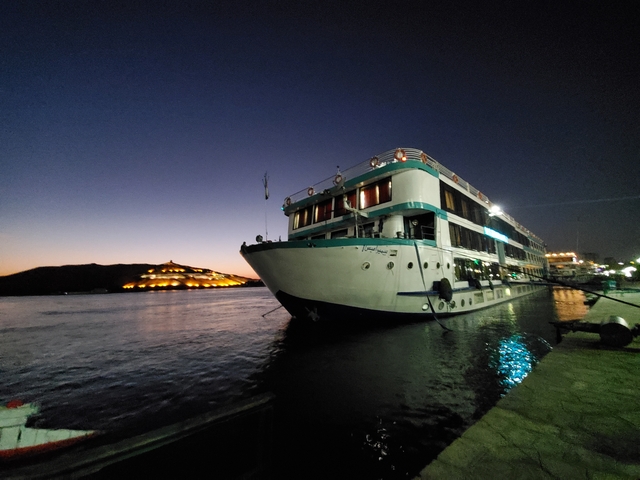 A ship docked at night with lights in the background.
