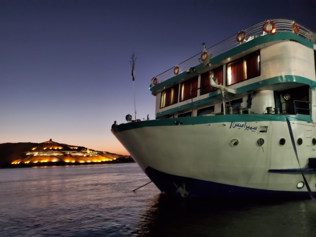 A boat in the foreground with a lit building in the background at dusk.