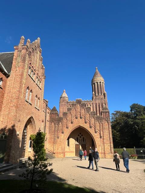       A historic brick building with towers and people walking around.
  