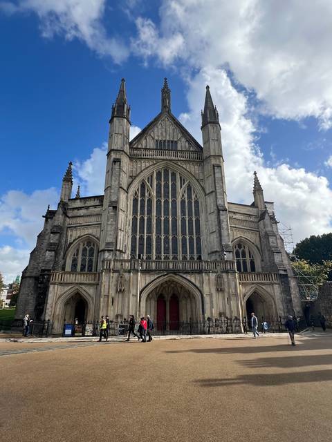       Gothic cathedral with pointed arches and stained glass windows, people walking in front
  