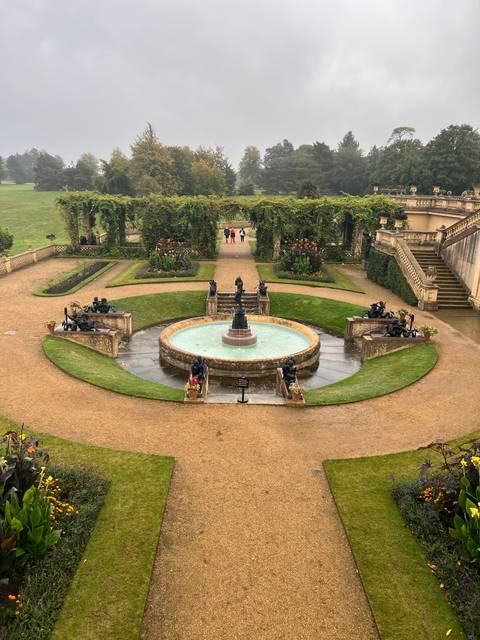       Fountain surrounded by gardens and pathways with people walking around
  