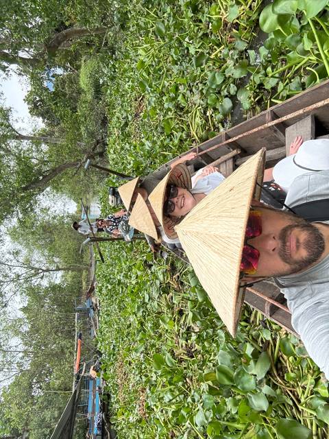 People in a boat with traditional hats navigating through greenery.