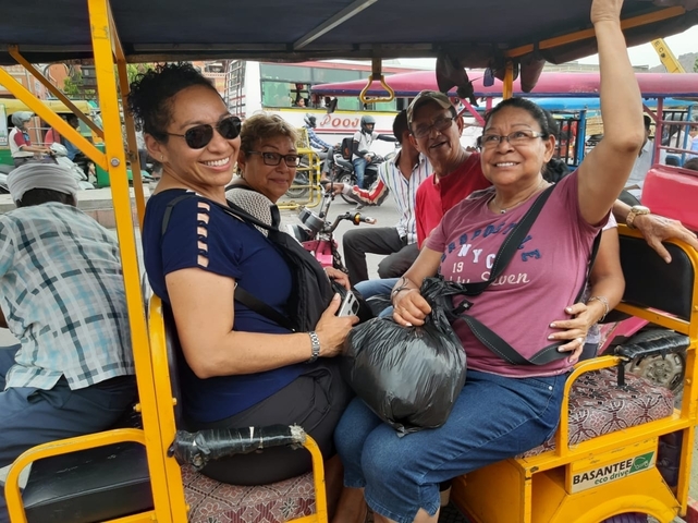 Group of people in a tuk tuk, smiling and waving.