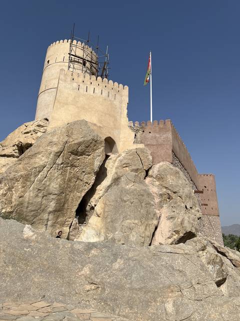       Historic fort with rugged rock faces and an Oman flag.
  