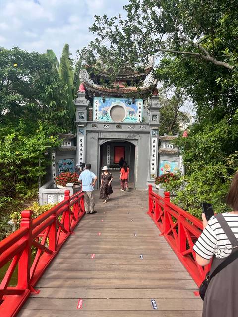       People crossing a red bridge towards a temple.
  