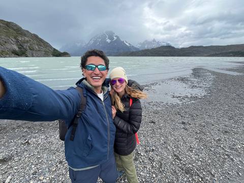 Couple taking a selfie on a rocky beach with mountains in background.