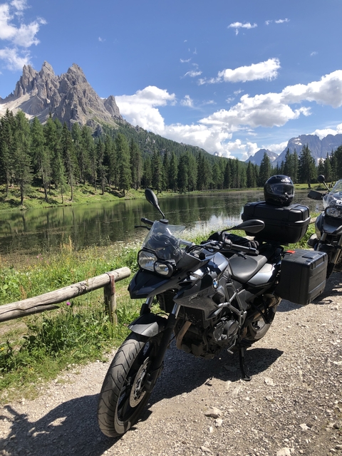 Motorcycles parked by a tranquil lake surrounded by trees.